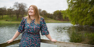 Hannah leaning against fence in front of lake.