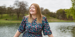 Hannah leaning against fence in front of lake.