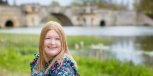 Close up of Hannah with a lake and stone bridge out of focus.