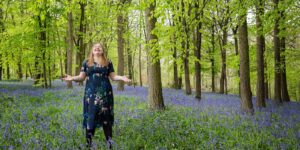 Hannah with arms spread out in bluebell woods.