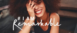 Women smiling with a hand over her face. #IamRemarkable